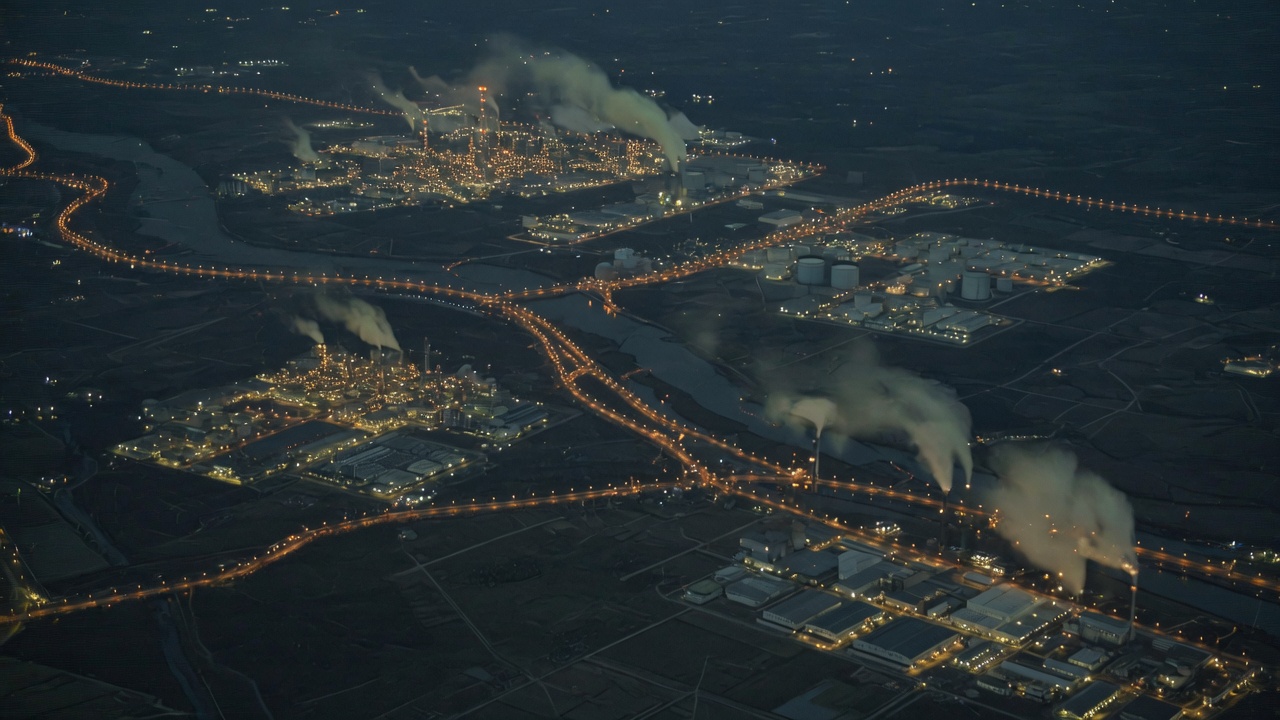 Nighttime aerial of industrial lights and faint plumes across dark land